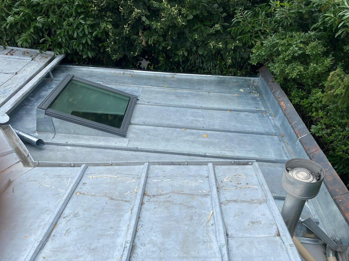 Couverture en zinc à joint debout sur toiture à faible pente, avec verrière encastrée, chapeau de ventilation et relevés en zinc en périphérie