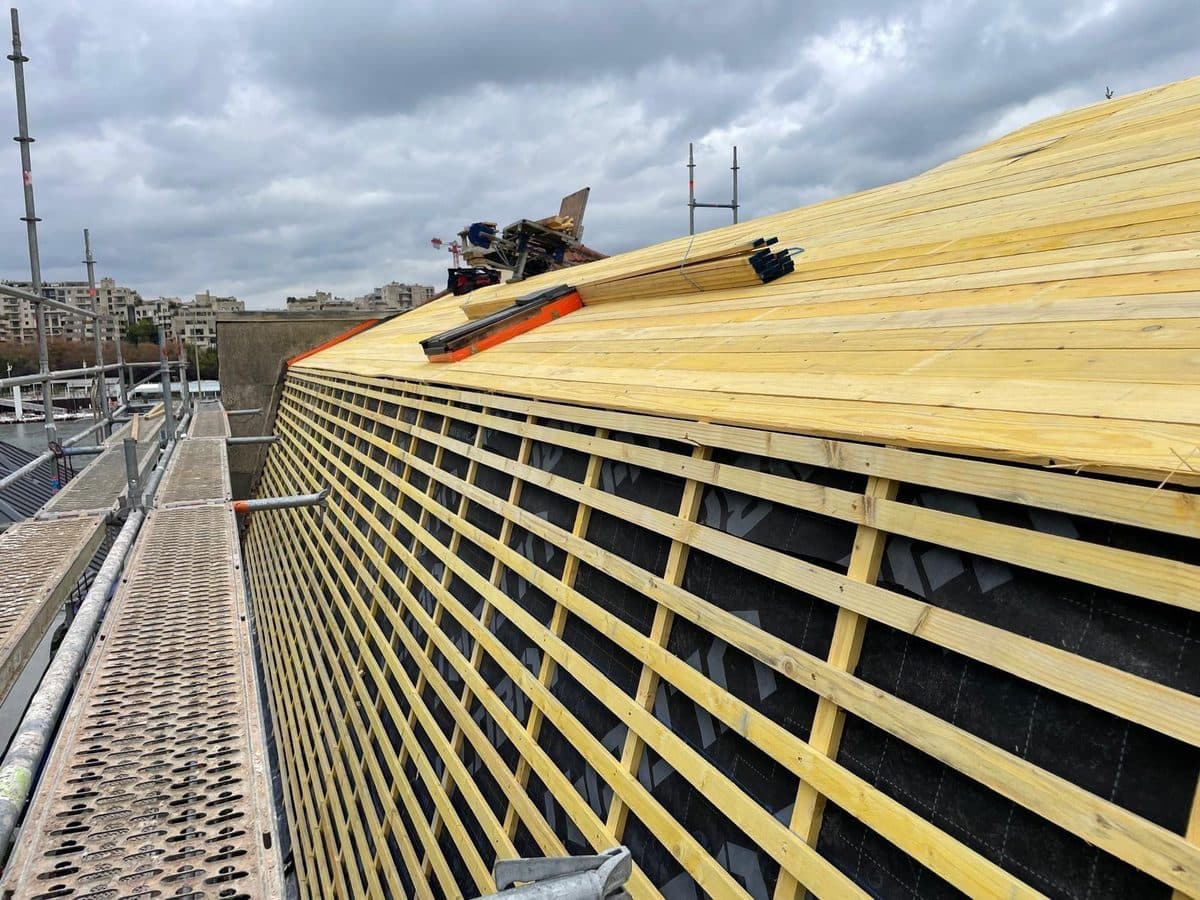 Liteaunage neuf en bois posé sur un écran de sous-toiture noir, avec voliges au faîtage, vu depuis l'échafaudage de chantier
