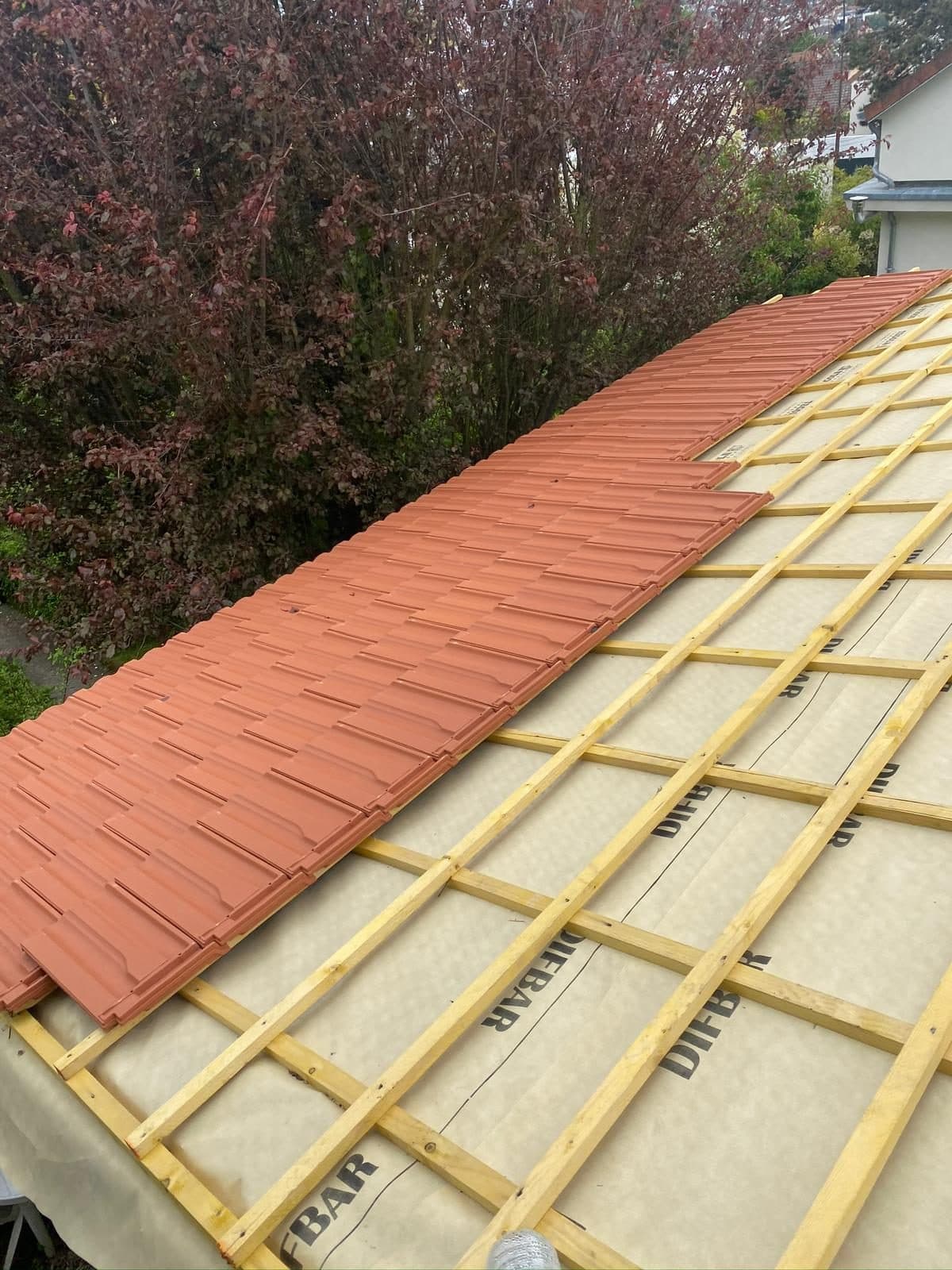 Premiers rangs de tuiles neuves posés sur le liteaunage et le contre-lattage d'une toiture, le reste de l'écran de sous-toiture encore visible